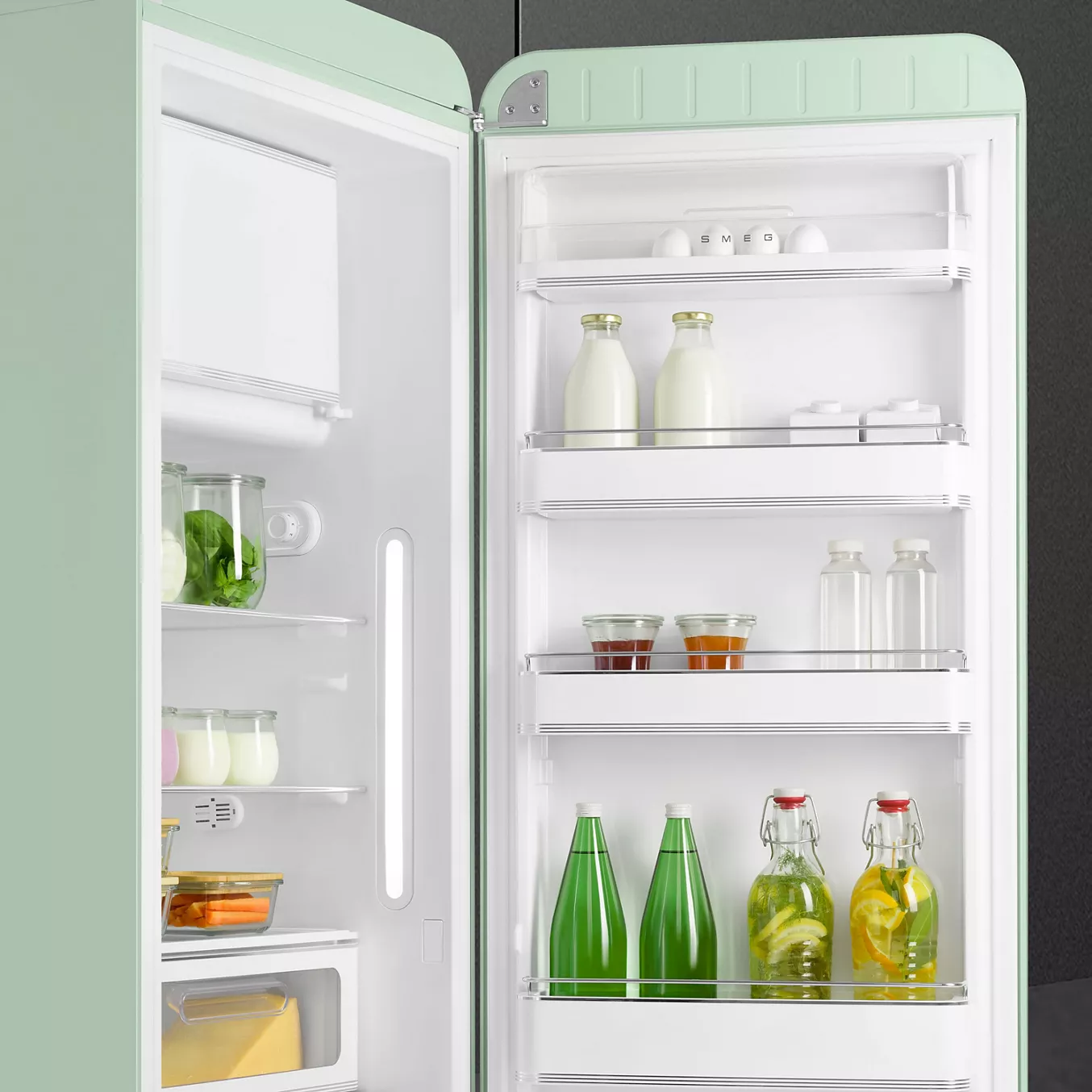 Le réfrigérateur rétro SMEG FAB28RPG6 vert menthe est ouvert et présente des boissons, du lait, des bocaux et des produits frais bien rangés sur ses étagères.