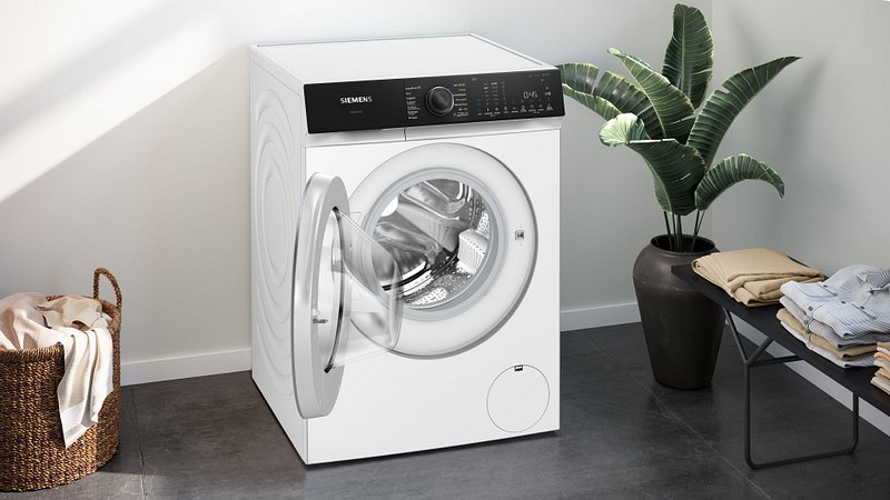 Le SIEMENS WG56H2A5FR, un lave-linge blanc à chargement frontal, est présenté avec sa porte ouverte dans une buanderie moderne.
