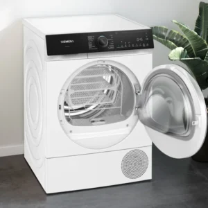 Un sèche-linge à chargement frontal SIEMENS WQ46H2CAFR blanc avec la porte ouverte, placé à côté d'une plante, d'un panier à linge et de vêtements pliés.