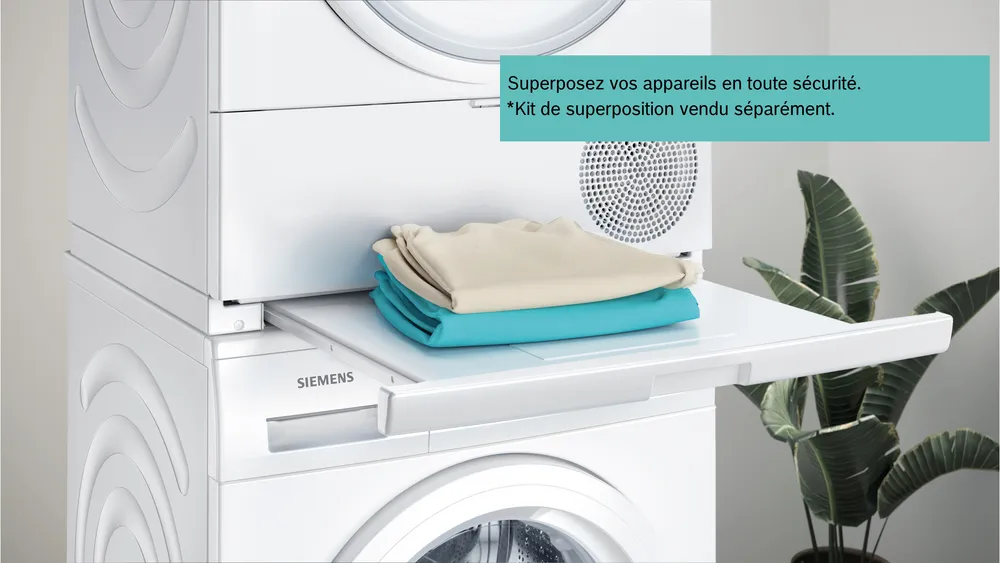 Une pile de linge plié est posée sur une étagère coulissante entre des appareils SIEMENS WQ46H2CAFR empilés, soulignant l'efficacité et le design moderne de ces appareils Siemens.