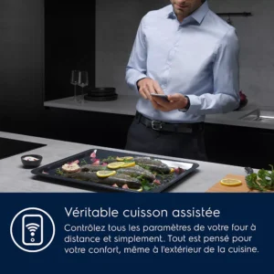 Un homme utilise son téléphone près d'un plateau de poisson et de légumes dans une cuisine moderne, vérifiant que le four ELECTROLUX COD6P46X0 (Copie) donne des résultats de cuisson parfaits.