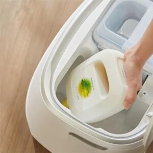 Une main place une bouteille de détergent NARWAL dans un compartiment d'une machine à laver blanche.