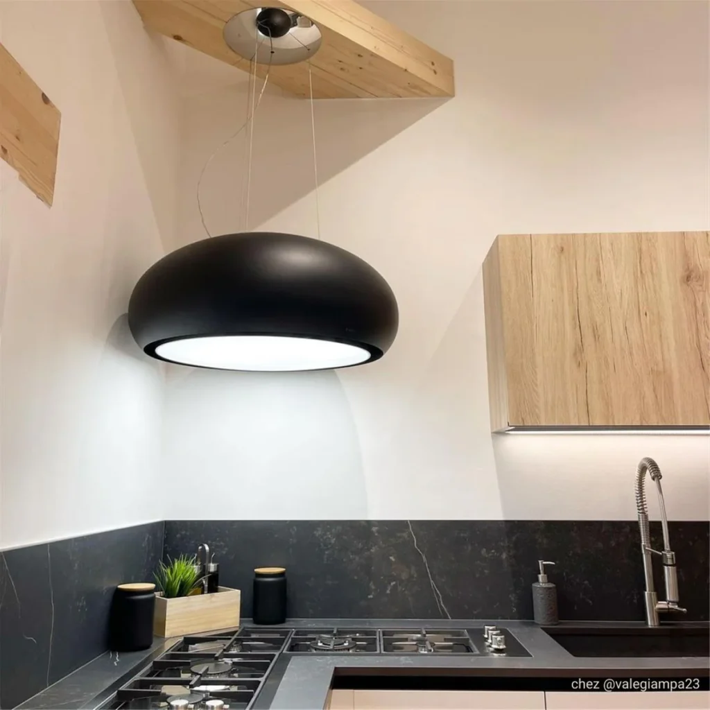 Cuisine moderne avec une grande lampe suspendue noire, des armoires en bois et une cheminée ELICA CRUISE IX/A/90 (Copie) au-dessus de la cuisinière à gaz pour une ventilation efficace.