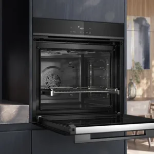 Le four encastrable SIEMENS HB472G0B3F est présenté avec sa porte ouverte dans une cuisine élégante remplie de lumière naturelle et d'élégantes touches de bois.