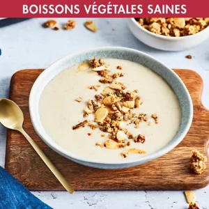 Un bol de soupe crémeuse réalisée avec la MAGIMIX 11628, garnie de granola sur une planche en bois, accompagnée d'une cuillère en or.