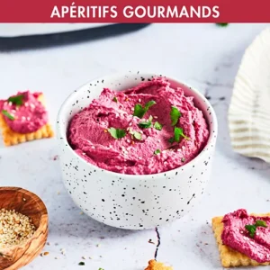 Houmous de betterave rose réalisé avec le MAGIMIX 11628, agrémenté d'herbes et servi avec des crackers et des graines de sésame dans un bol moucheté.