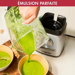 Une main verse de la soupe verte d'un mixeur MAGIMIX 11628 dans un bol, à côté d'un autre bol rempli et de tranches de pain.