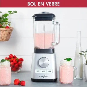Un mixeur MAGIMIX 11630 argenté avec un pichet en verre mixe un smoothie rose, entouré de fraises fraîches et de pots de smoothie.