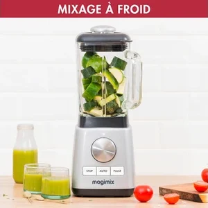 Un mixeur MAGIMIX 11630, rempli de légumes hachés, est entouré de jus vert, de tomates et d'un concombre.