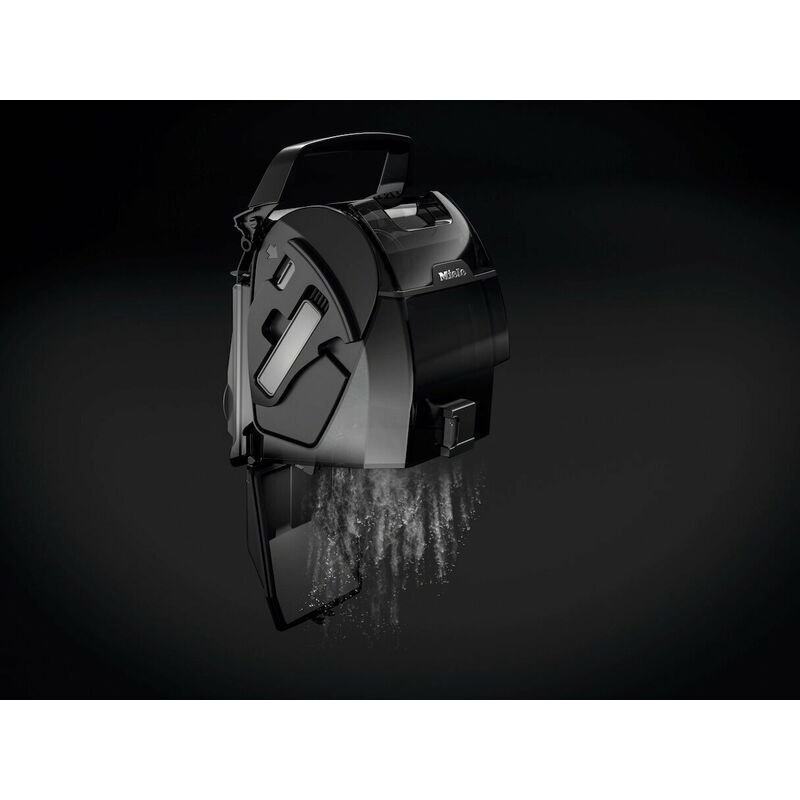 Le bac à poussière de l'aspirateur Miele BOOST CX1 POWERLINE libère des débris sur un fond sombre.