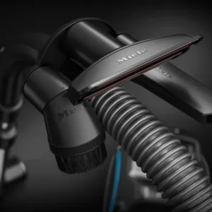 Gros plan du tuyau de l'aspirateur Miele BOOST CX1 POWERLINE avec la brosse et le suceur plat attachés, mis en évidence sur un fond sombre pour un look élégant.