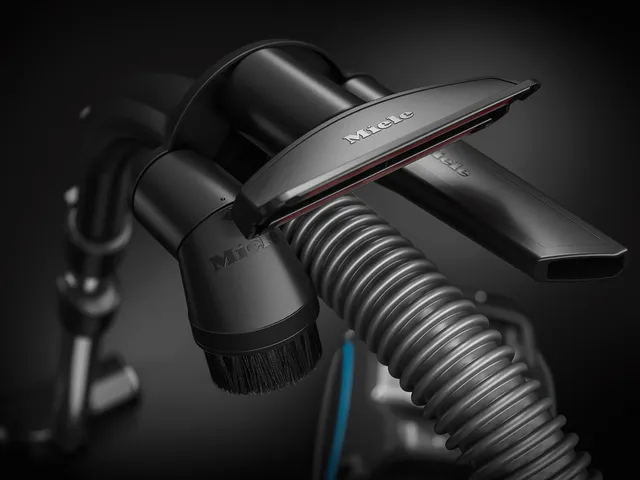 Gros plan du tuyau de l'aspirateur Miele BOOST CX1 POWERLINE avec la brosse et le suceur plat attachés, mis en évidence sur un fond sombre pour un look élégant.