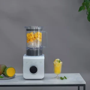 Un mixeur SMEG BLC01BLMEU rempli de cubes de mangue est posé sur une table en marbre à côté d'un verre de smoothie à la mangue.