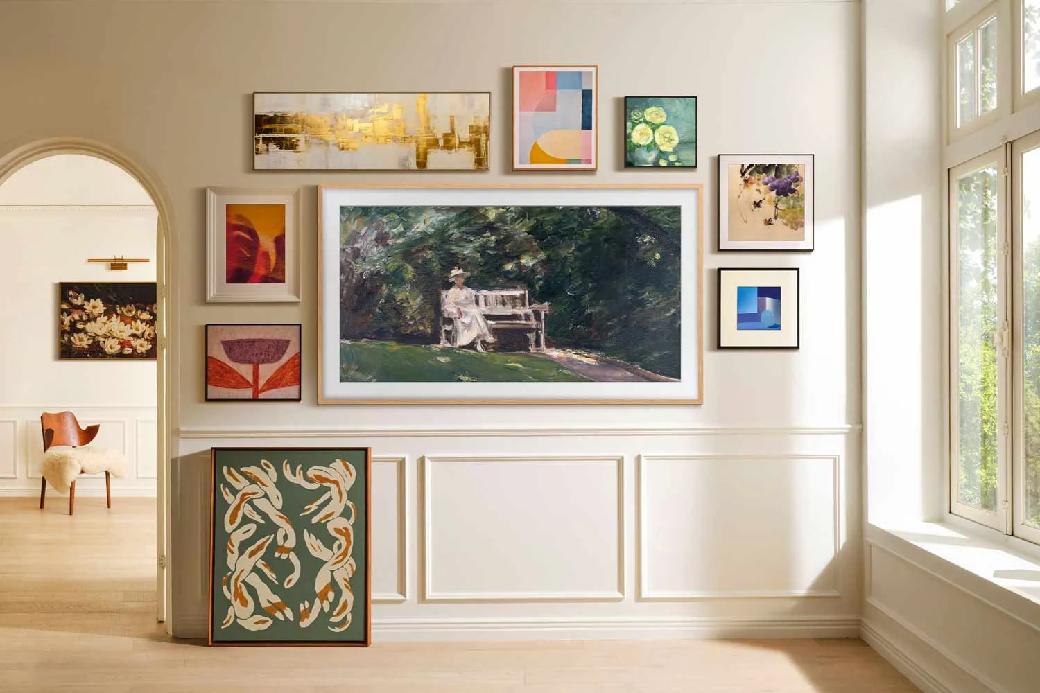 Un mur d'art encadré au-dessus de panneaux blancs dans une pièce lumineuse, mettant en valeur le téléviseur SAMSUNG TQ65LS03WF qui s'intègre parfaitement à l'ensemble.