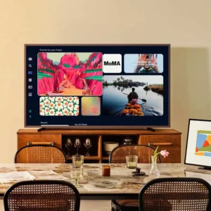Un téléviseur intelligent SAMSUNG TQ65LS03WF est placé sur un meuble en bois dans la salle à manger, mettant en valeur des œuvres d'art vibrantes et des choix de streaming.