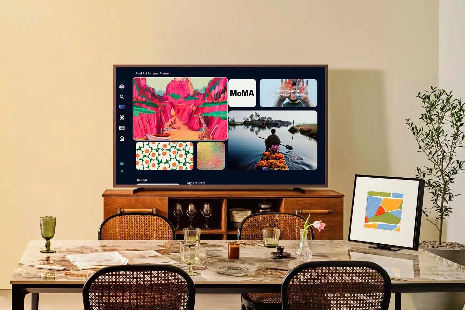 Un téléviseur intelligent SAMSUNG TQ65LS03WF est placé sur un meuble en bois dans la salle à manger, mettant en valeur des œuvres d'art vibrantes et des choix de streaming.