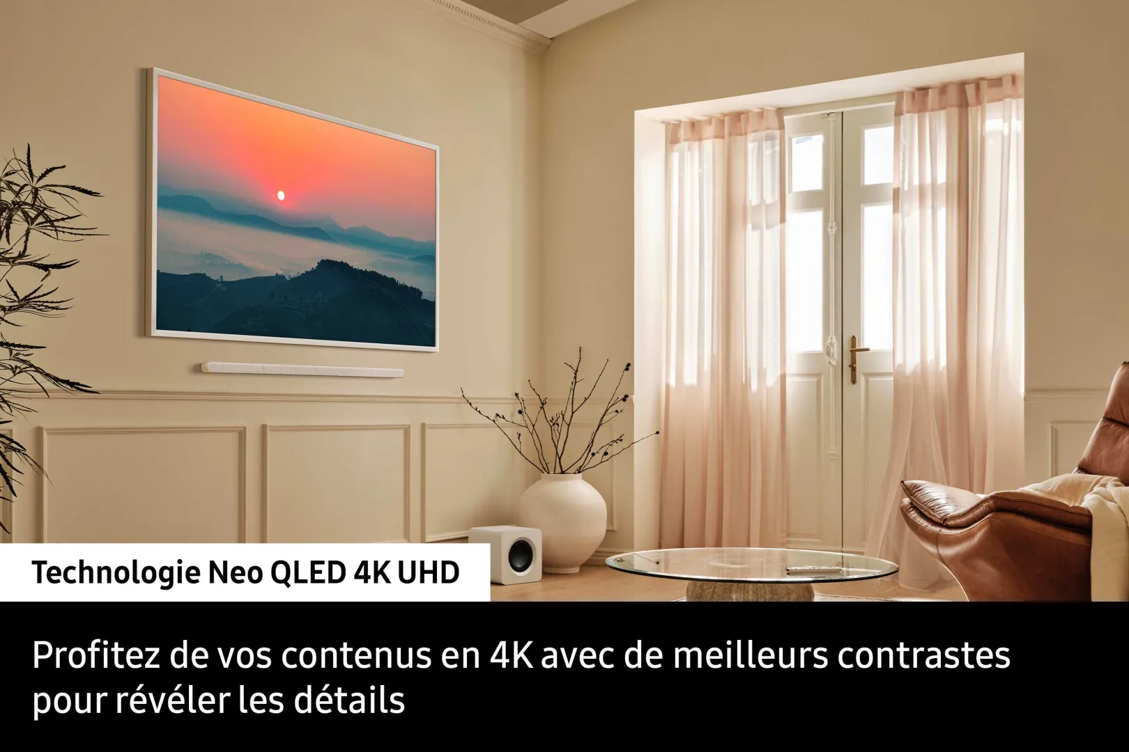 Dans un salon moderne, un téléviseur mural SAMSUNG TQ65LS03WF affiche une scène de coucher de soleil avec un texte en français mettant en valeur sa technologie 4K QLED UHD.