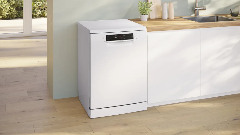 Un lave-vaisselle BOSCH SMS25AW10F se trouve à côté d'un plan de travail de cuisine blanc comprenant un comptoir en bois et un évier.