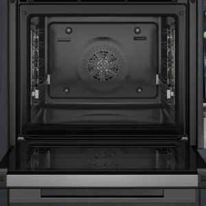 Four SIEMENS HB472G0B3 ouvert, à l'intérieur noir, placé à côté d'un plan de travail en marbre décoré de livres de cuisine et de vases élégants.
