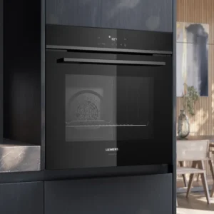 Le four encastrable SIEMENS HB472G0B3 ajoute style et fonctionnalité à une cuisine moderne aux accents de bois, éclairée par la lumière du soleil à travers de grandes fenêtres.