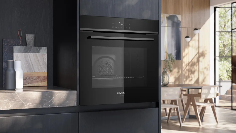 Le four encastrable SIEMENS HB472G0B3 ajoute style et fonctionnalité à une cuisine moderne aux accents de bois, éclairée par la lumière du soleil à travers de grandes fenêtres.