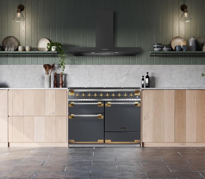 Cuisine moderne avec armoires en bois clair, cuisinière FALCON ELS110EIGB/BE-EU noir et or, dosseret en marbre et murs vert foncé.