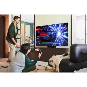 Deux personnes jouent à un jeu de course sur un téléviseur SAMSUNG TQ77s92f dans un salon moderne pendant qu'une autre personne regarde.