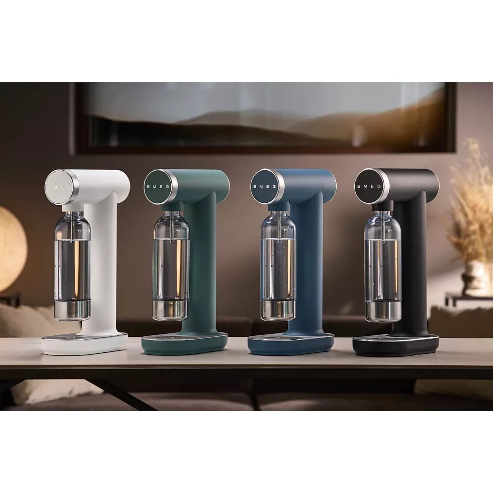 Quatre machines à soda SMEG, dont la SKC01BLM NOIR MAT, ainsi que des modèles en blanc, vert et bleu, sont exposées ensemble à l'intérieur.