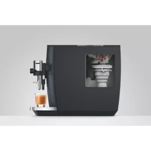Vue latérale de la machine à café JURA E8 COSMIC BLACK (ED) préparant un espresso frais dans une tasse en verre transparent.