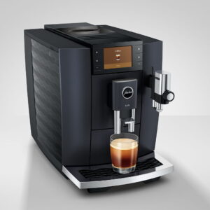 La machine à café JURA E8 COSMIC BLACK (ED) verse sans effort un café riche dans une tasse en verre placée sur son plateau, sur un fond uni.
