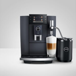 Un JURA E8 COSMIC BLACK (ED) est assis sur une surface blanche avec un récipient à lait, préparant un café au lait, sur un fond gris.