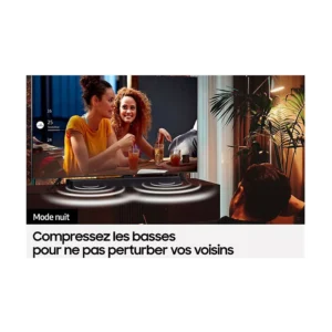 La nuit, un homme regarde la télévision avec la barre de son SAMSUNG HW-C450, tandis que deux femmes sourient et parlent à l'écran ; un texte en français sur la réduction des basses apparaît.