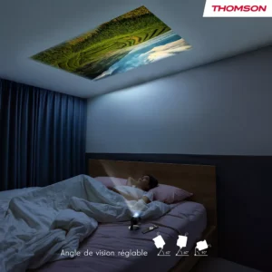Détendu dans son lit, quelqu'un regarde une scène de nature au plafond, projetée par le THOMSON VEGA PG35B compact placé sur sa table de chevet.