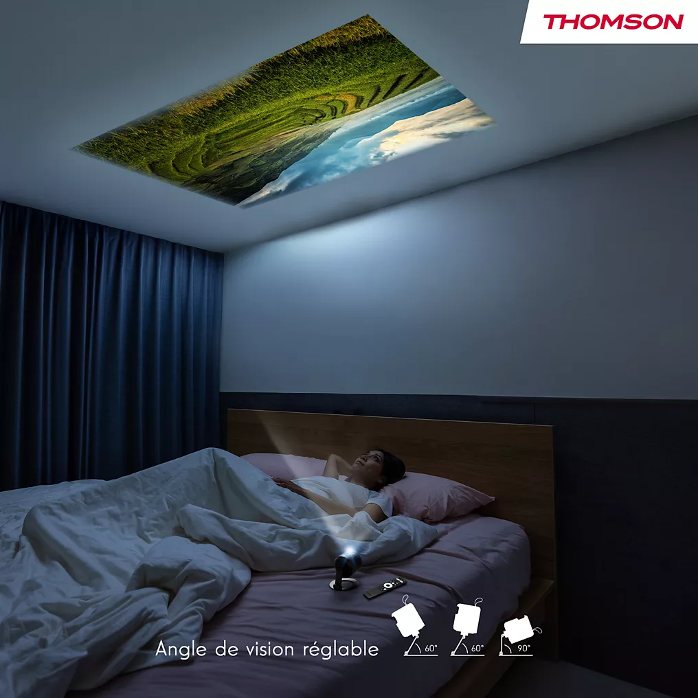 Détendu dans son lit, quelqu'un regarde une scène de nature au plafond, projetée par le THOMSON VEGA PG35B compact placé sur sa table de chevet.