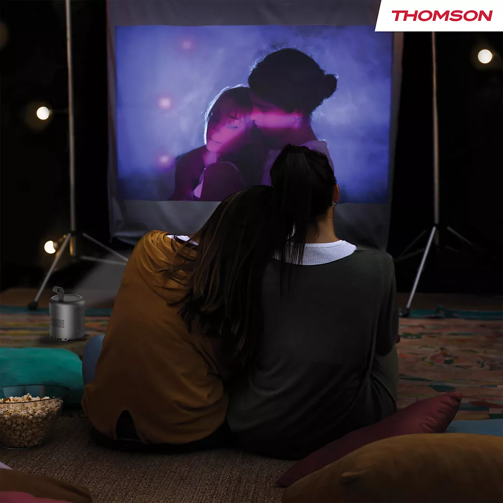 Deux personnes sont assises l'une près de l'autre et regardent un film en plein air la nuit. Le logo THOMSON VEGA PG35B est visible dans le coin.