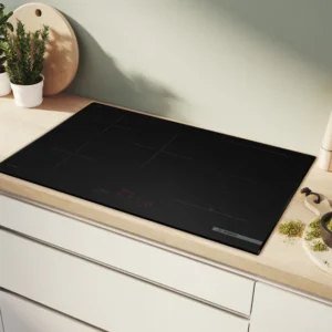 Cuisine moderne équipée de la table de cuisson à induction BOSCH PVW89BHC1E en noir, complétée par des herbes fraîches et des ustensiles sur un plan de travail en bois clair.