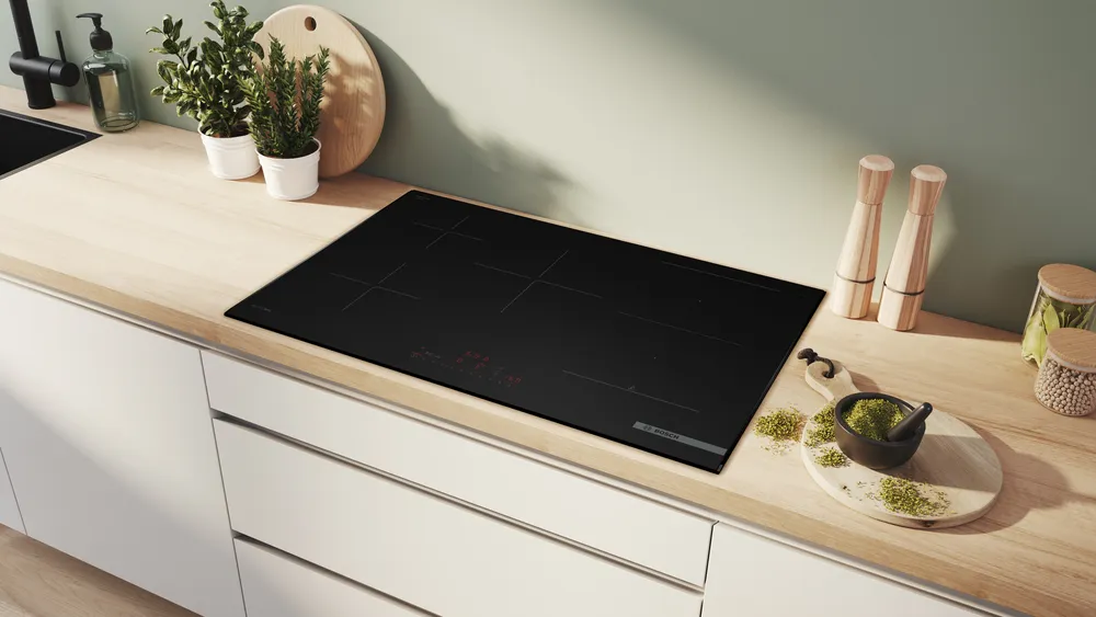 Cuisine moderne équipée de la table de cuisson à induction BOSCH PVW89BHC1E en noir, complétée par des herbes fraîches et des ustensiles sur un plan de travail en bois clair.