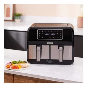 Une friteuse KENWOOD HFM20.000MB à double panier est posée sur le comptoir de la cuisine à côté d'une assiette contenant du poulet et des légumes.