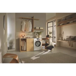 Une femme s'agenouille pour charger du linge dans un lave-linge MIELE WSG883WCS dans une buanderie moderne et élégante.
