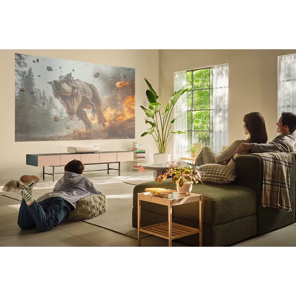 Une famille regarde un film d'action sur les dinosaures sur un grand écran dans leur salon moderne et lumineux, projeté par le SAMSUNG SP-PLU7D.