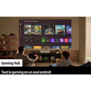 Deux personnes sont assises sur un canapé pour jouer, face à un grand écran montrant le SAMSUNG SP-PLU7D avec le menu Samsung Gaming Hub affiché.