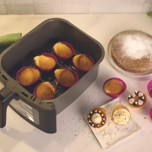 Des mini cupcakes et un gâteau sont posés sur un comptoir, et quelques cupcakes sont placés dans le panier ouvert du FRIFRI AIRFRYER DUO SLIM.