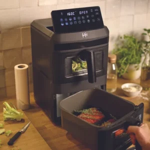Une personne utilise le FRIFRI AIRFRYER DUO SLIM pour faire cuire des légumes sur un comptoir de cuisine avec divers ustensiles de cuisine à proximité.