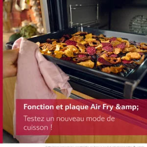Une main utilise un chiffon pour glisser un plateau de légumes secs colorés dans le four NEFF B2ACJ7AG0, en sélectionnant le mode Air Fry.