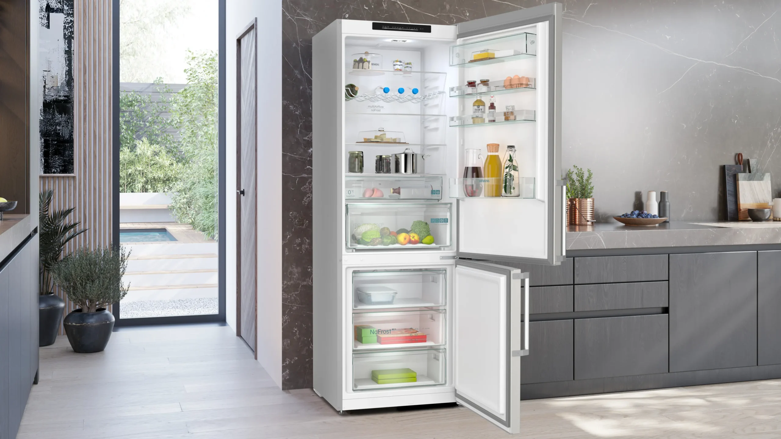 Une cuisine moderne présente un réfrigérateur-congélateur SIEMENS KG49NEICU ouvert et entièrement approvisionné, placé à côté d'armoires sombres et élégantes.