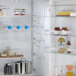 Ouvrez le réfrigérateur SIEMENS KG49NEICU pour découvrir des boissons, du fromage, des bocaux et des condiments bien rangés sur les étagères et dans la porte.