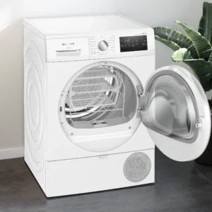 Un sèche-linge SIEMENS WT45H00MFR blanc avec sa porte ouverte est placé à côté d'une plante et de linge plié dans une pièce lumineuse.