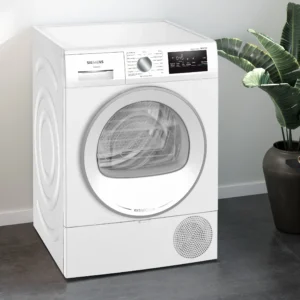 Un lave-linge SIEMENS WT45H00MFR à chargement frontal de couleur blanche trône dans une buanderie moderne, entouré d'une plante, d'un panier à linge et de vêtements soigneusement pliés.