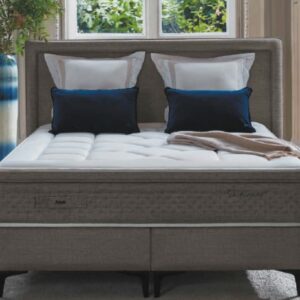 Un lit bien fait avec un matelas EPEDA GALACTIQUE 2 160x200, quatre oreillers, un jeté beige et une tête de lit tapissée grise dans une chambre lumineuse.