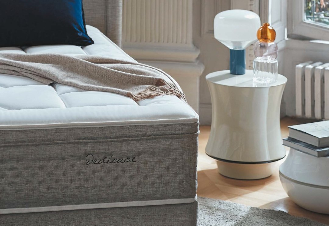 Un lit EPEDA GALACTIQUE 2 160x200, soigneusement confectionné avec un plaid beige, se trouve à côté d'une table de nuit moderne dotée de deux lampes et d'un décor en verre.